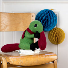 duck billed platypus soft toy in green and red on a chair